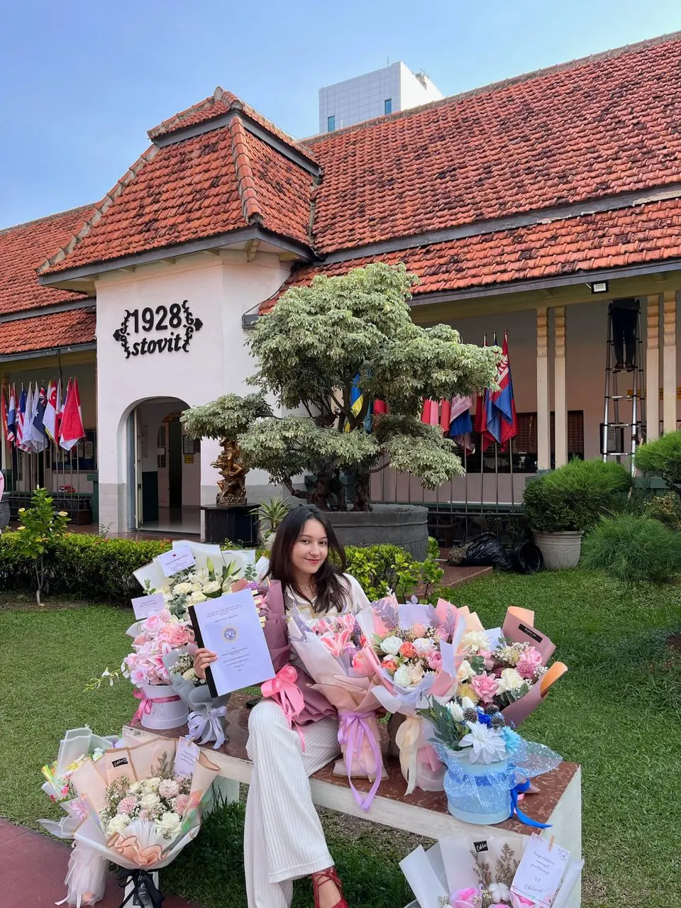 Gisele seated with graduation bouquets outside the dentistry faculty building.